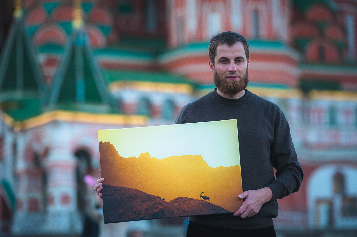 Фотограф Евгений Еремеев с холстом в руках на фоне Храма Василя Блаженного в Москве.