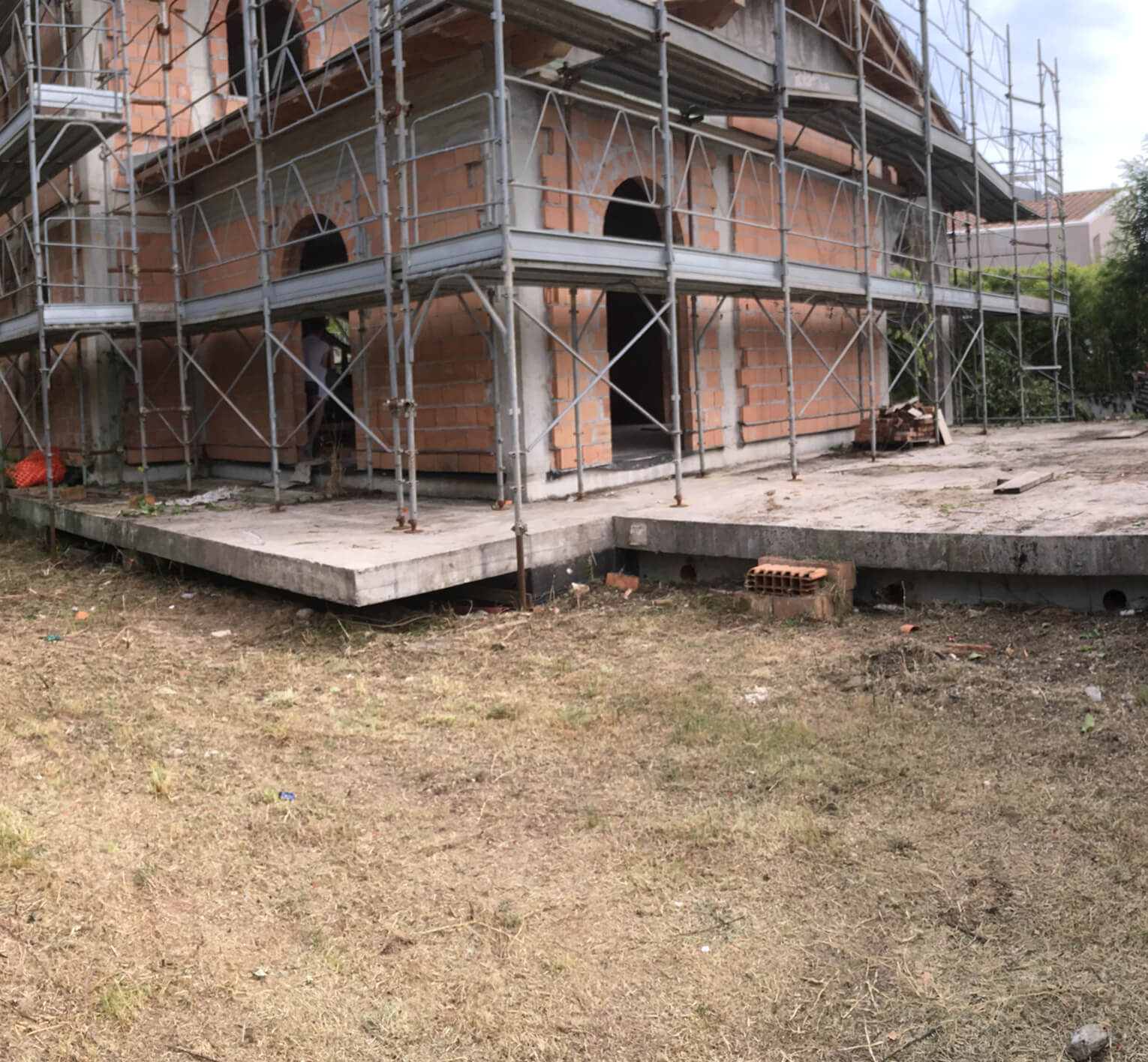 Villa development project in Forte dei Marmi showing concrete foundation, retaining walls, wooden structural frames, and construction site in progress.