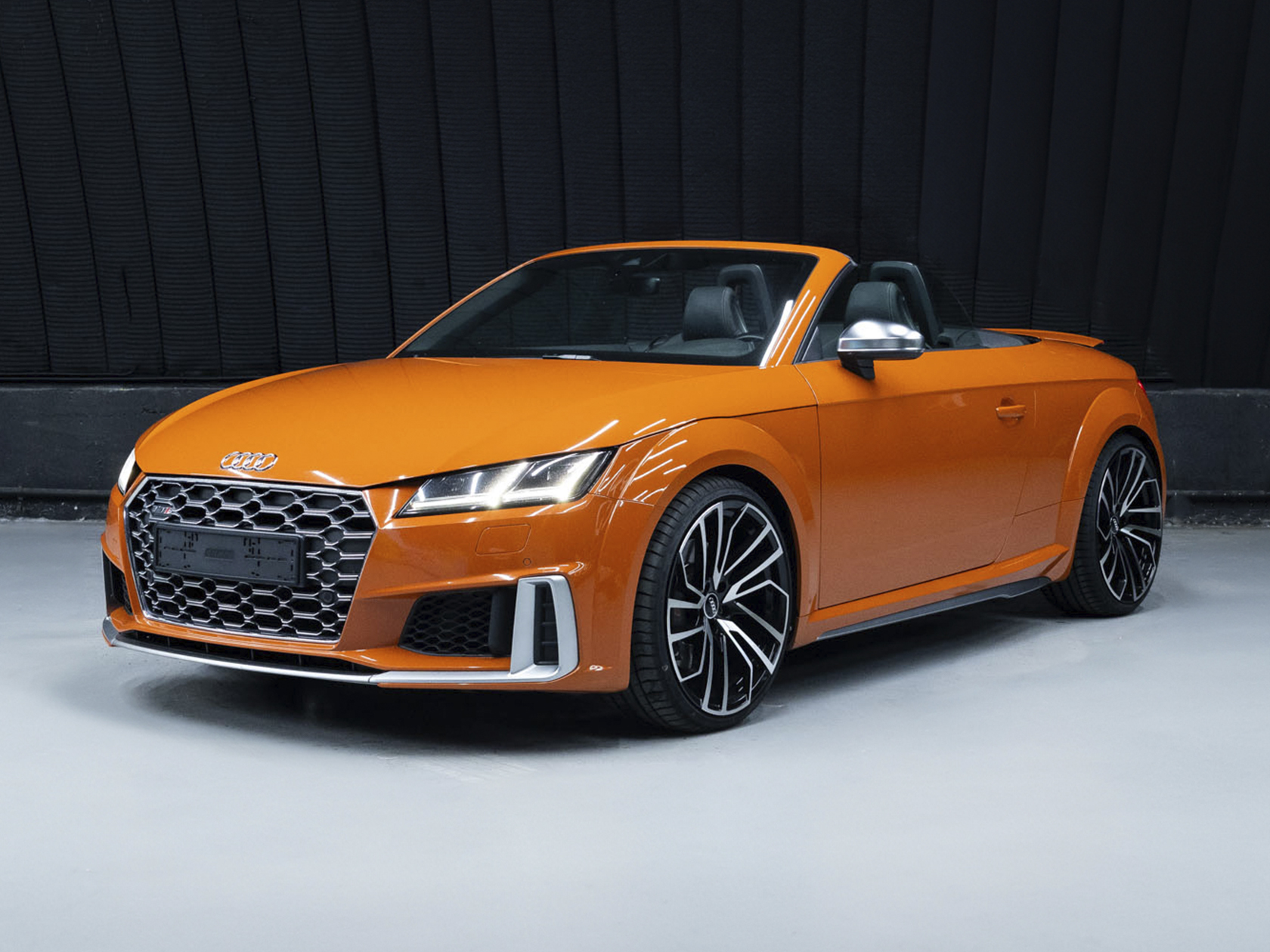 На данном изображении представлен автомобиль Audi TTs Roadster, воплощение стиля и динамичности. Этот роскошный родстер сочетает в себе элегантный дизайн и выдающиеся характеристики, обеспечивая увлекательный опыт вождения. Кузов автомобиля ярко оранжевого цвета, придающего ему смелость и индивидуальность. Динамичные линии и характерные черты дизайна Audi подчеркивают энергию и страсть этой модели, а уникальный оттенок морковного цвета делает TTs Roadster неповторимым и выделяет его на дороге. Эмблема Audi на передней решетке и задней части автомобиля говорит о превосходстве и технологическом инновационном подходе марки. Это изображение передает не только внешний вид автомобиля, но и обещание увлекательных вождения и стиля, а также выделение на фоне яркого оранжевого цвета, характерного для Audi TTs Roadster.