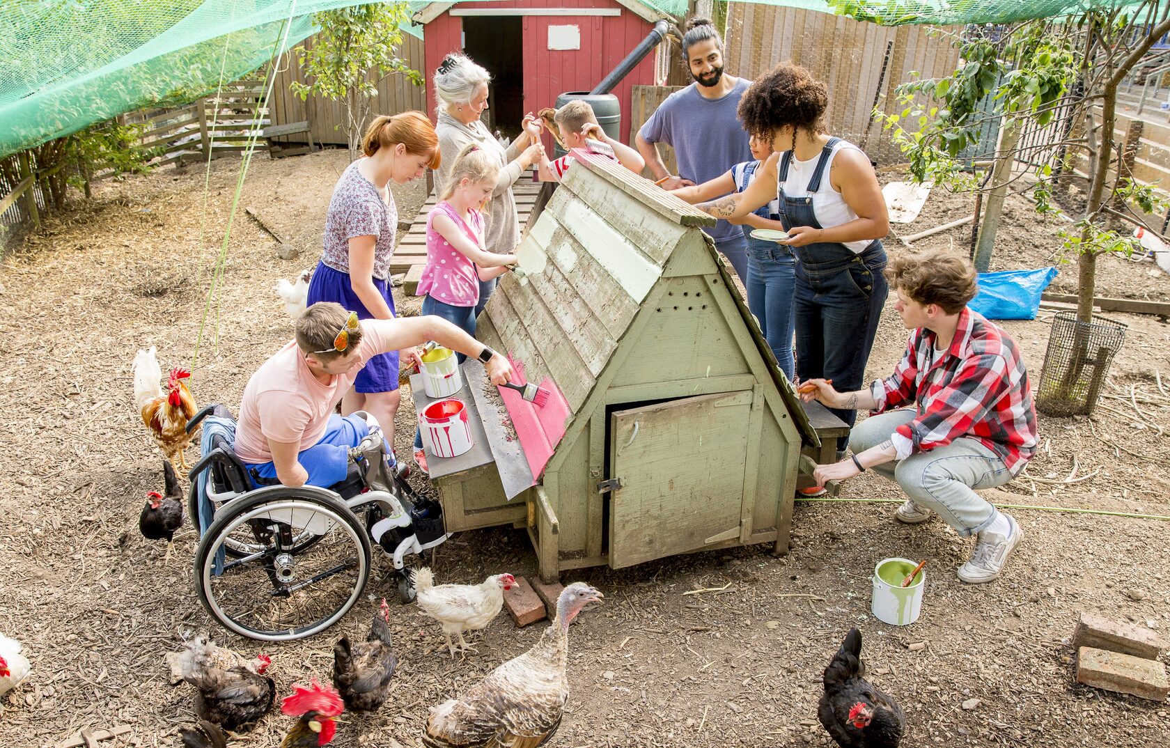An inclusive group of mixed ability and ethnicity children painting a chicken coup with adults in positions of trust